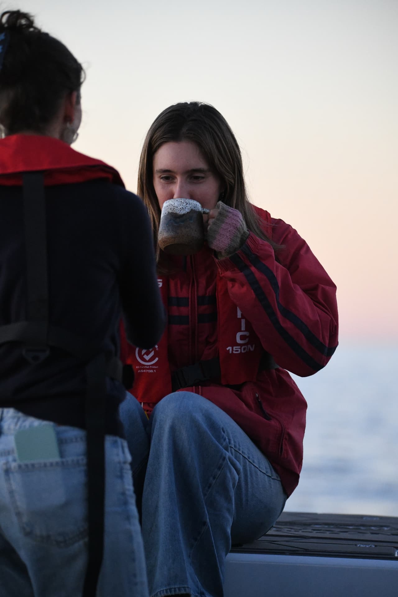 Guest warming up with a hot drink on deck at sunset during a Ballina voyage