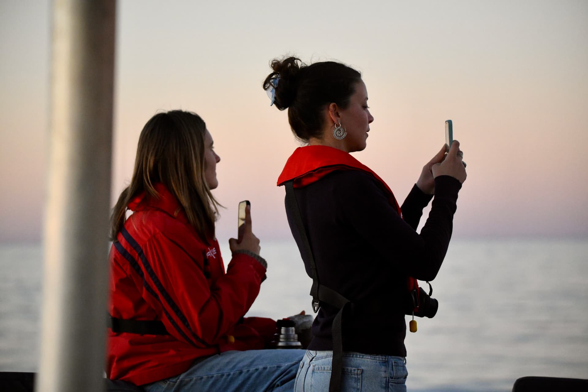 Two guests photographing the ocean at sunset aboard Cetacean One